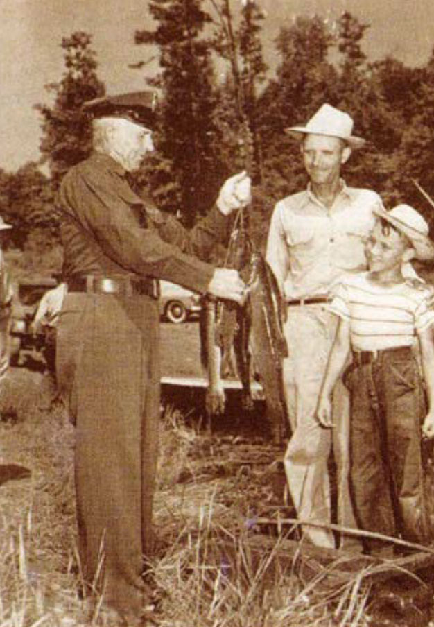 صورة بالأبيض والأسود لحارس صيد يحمل سمكة ويتحدث إلى شخصين