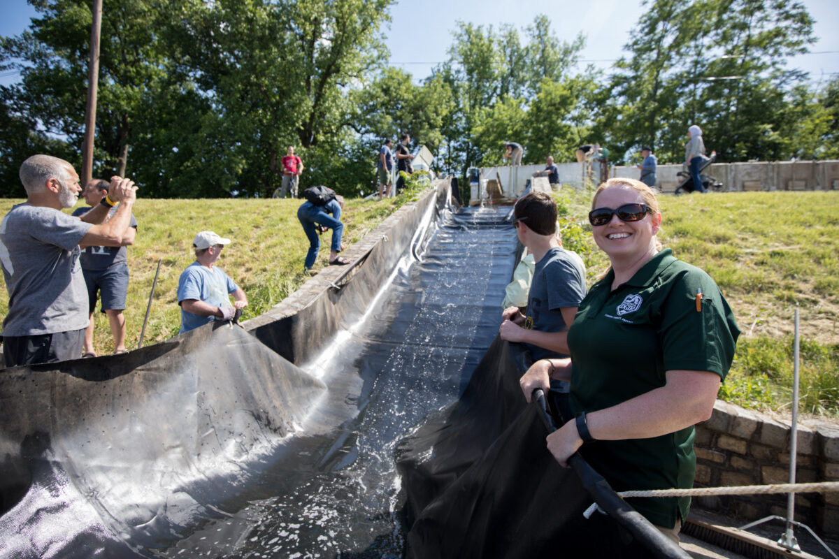 يساعد موظفو DWR والمتطوعون في تخزين الأسماك في بحيرة شيلد، من خلال حمل قماش القنب المملوء بالماء لتوجيه خزانات الأسماك المصبوبة في البحيرة