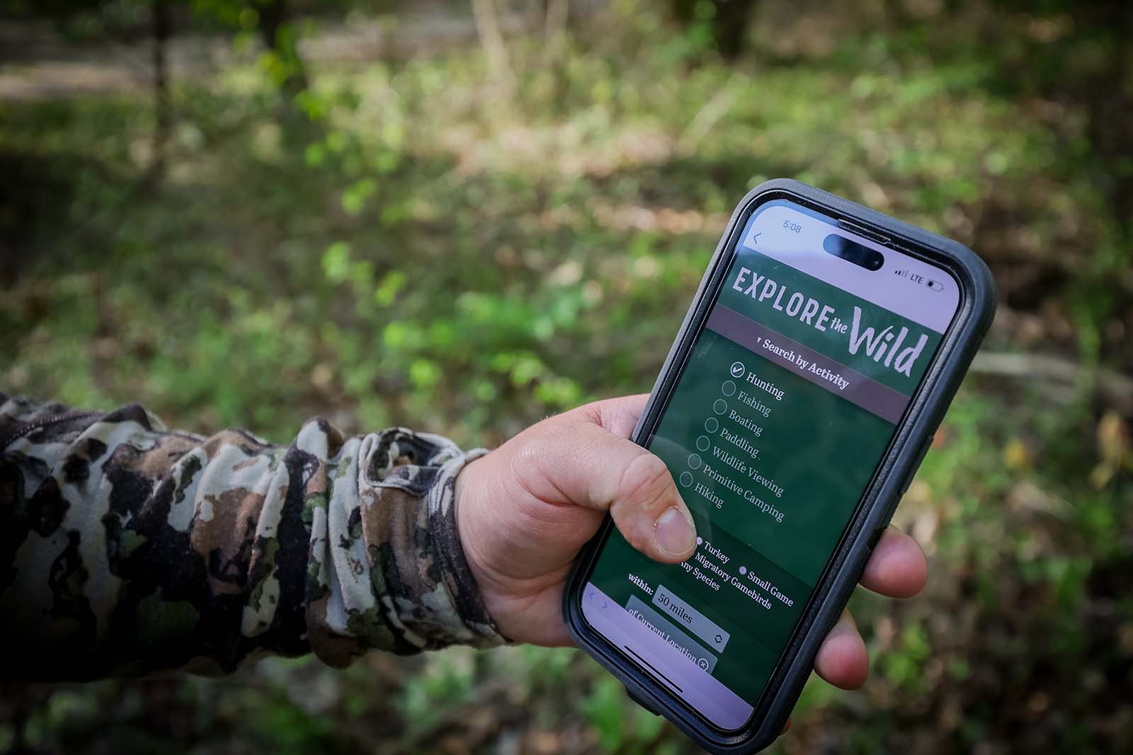 يد تحمل هاتفًا ذكيًا مع عرض استكشف البرية
