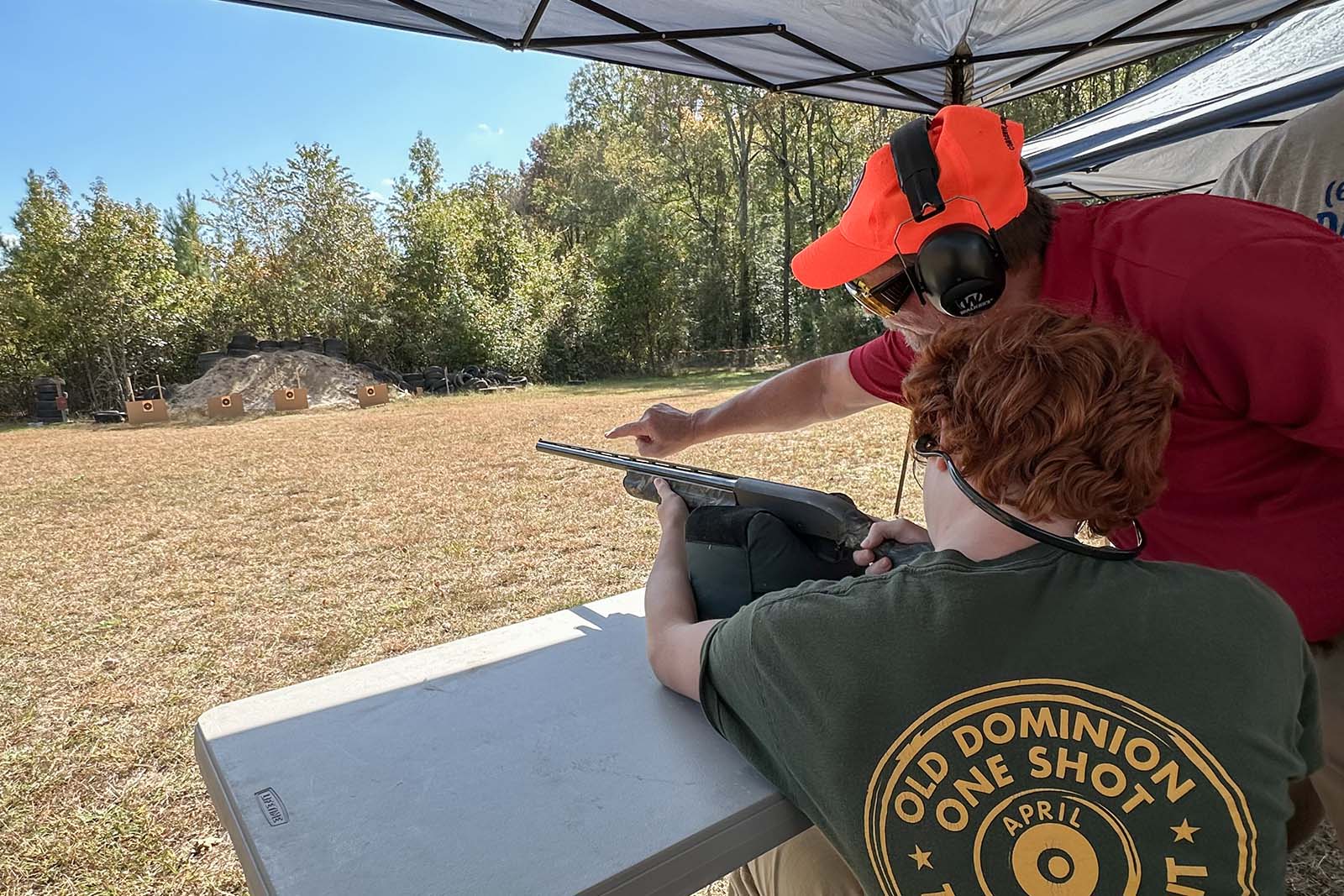 شخص يتدرب على التصويب على الأهداف ببندقية صيد؛ ويقف مدرب بالقرب منه يشير إلى الهدف