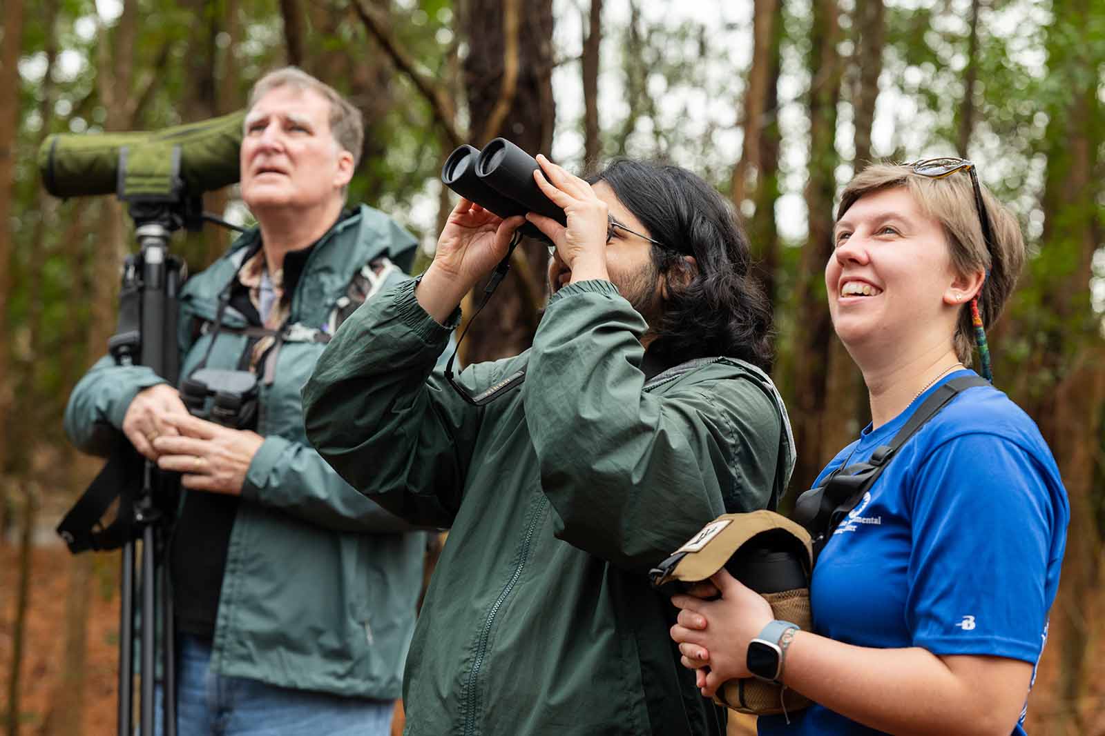 شخصان يرتديان سترة خضراء داكنة وينظران إلى أعلى، أحدهما يستخدم منظاراً معظماً