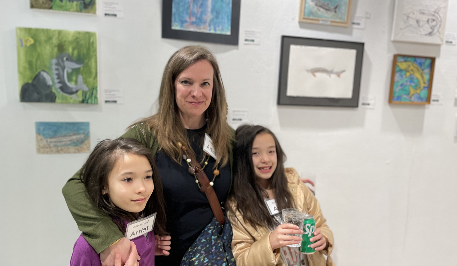 صورة لامرأة وطفلتين 8-عمرهما -عمرهما تقفان أمام حائط مليء باللوحات.