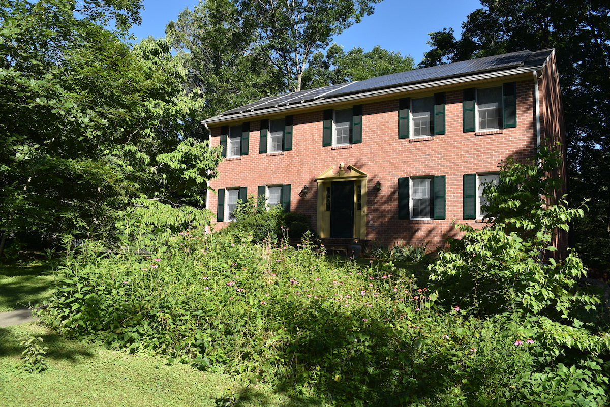 صورة لمنزل من الطوب مع ألواح شمسية على السطح وحديقة ملقحات في الفناء الأمامي