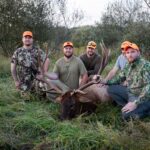 خمسة رجال يقفون مع ظبي نافق، محاطين بأشجار متناثرة.