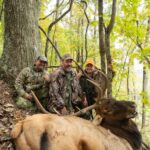 ثلاثة رجال في الغابة يقفون مع صيدهم من الأيائل.