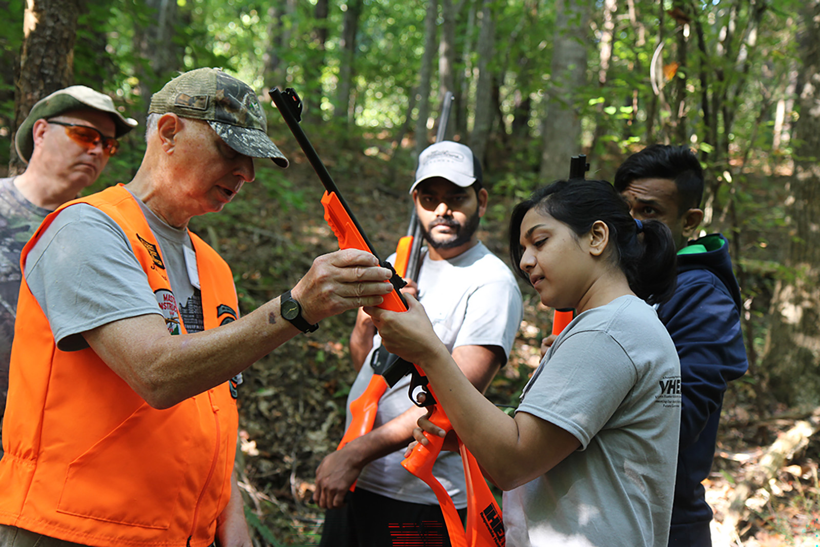 صورة لرجل يشرح كيفية حمل بندقية لامرأة بينما تنظر المجموعة.