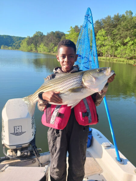 صبي صغير، عمره 6 ، يحمل سمكة كبيرة بين ذراعيه على متن قارب.