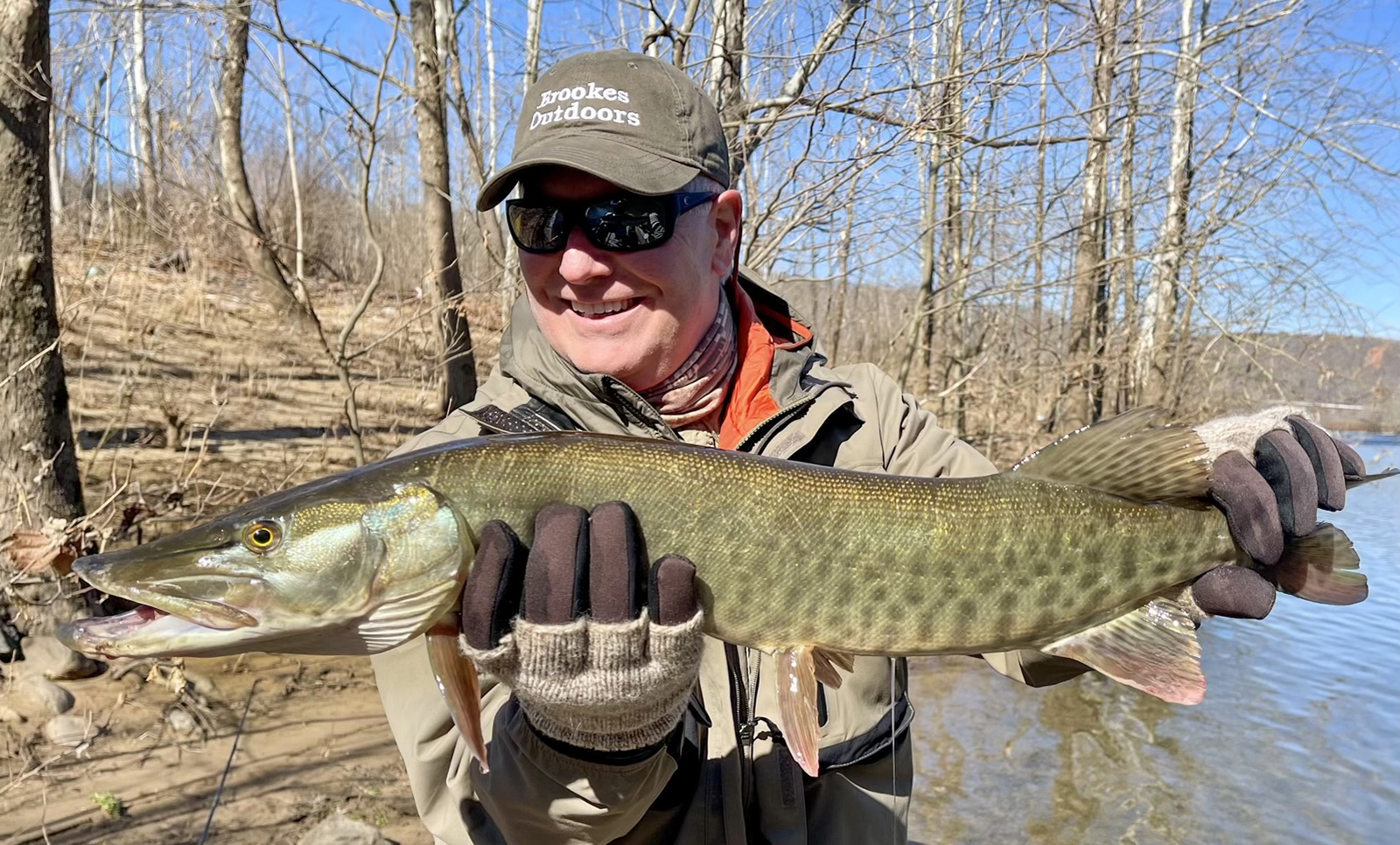 صورة لرجل يحمل سمكة مسكية كبيرة خارج الماء ويبتسم.