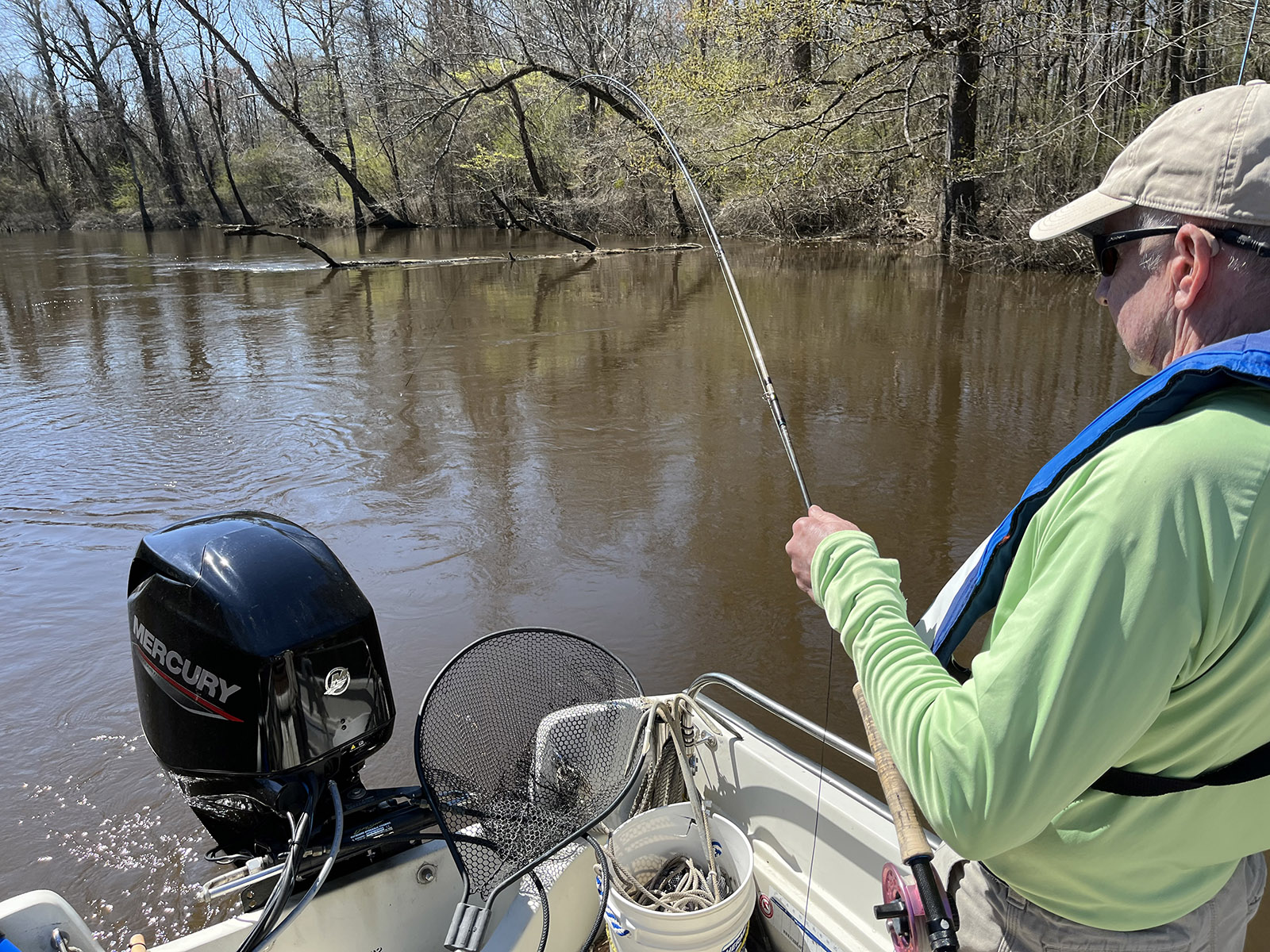 صورة لرجل يقف في قارب مع صنارة صيد ذبابة منحنية فوق الماء.