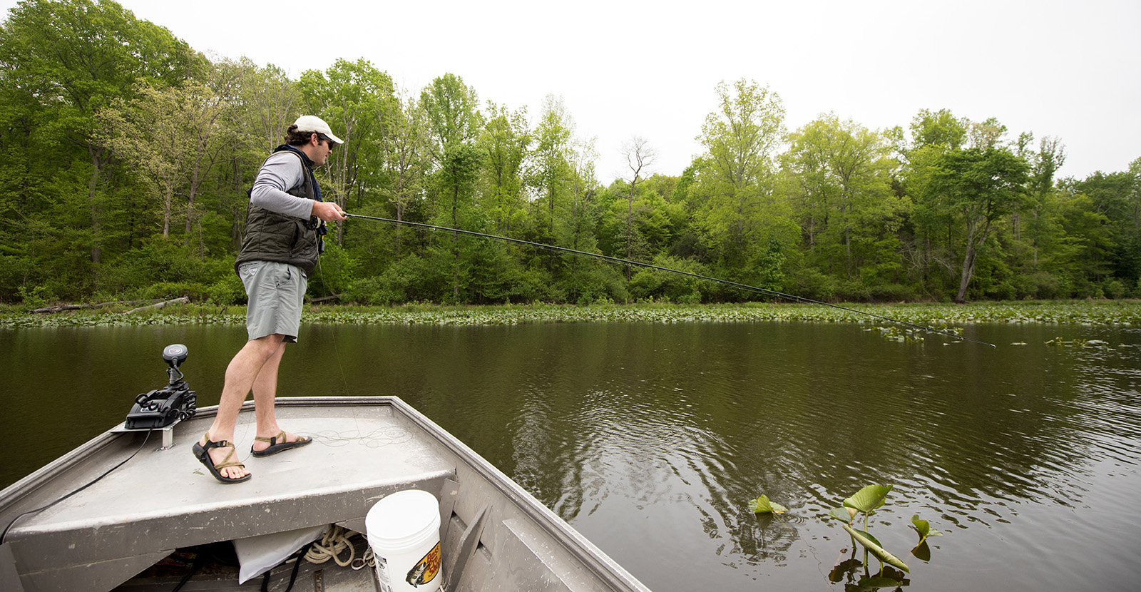 رجل يقف في مقدمة قارب صيد ممسكاً بصنارة صيد وينظر إلى الماء.