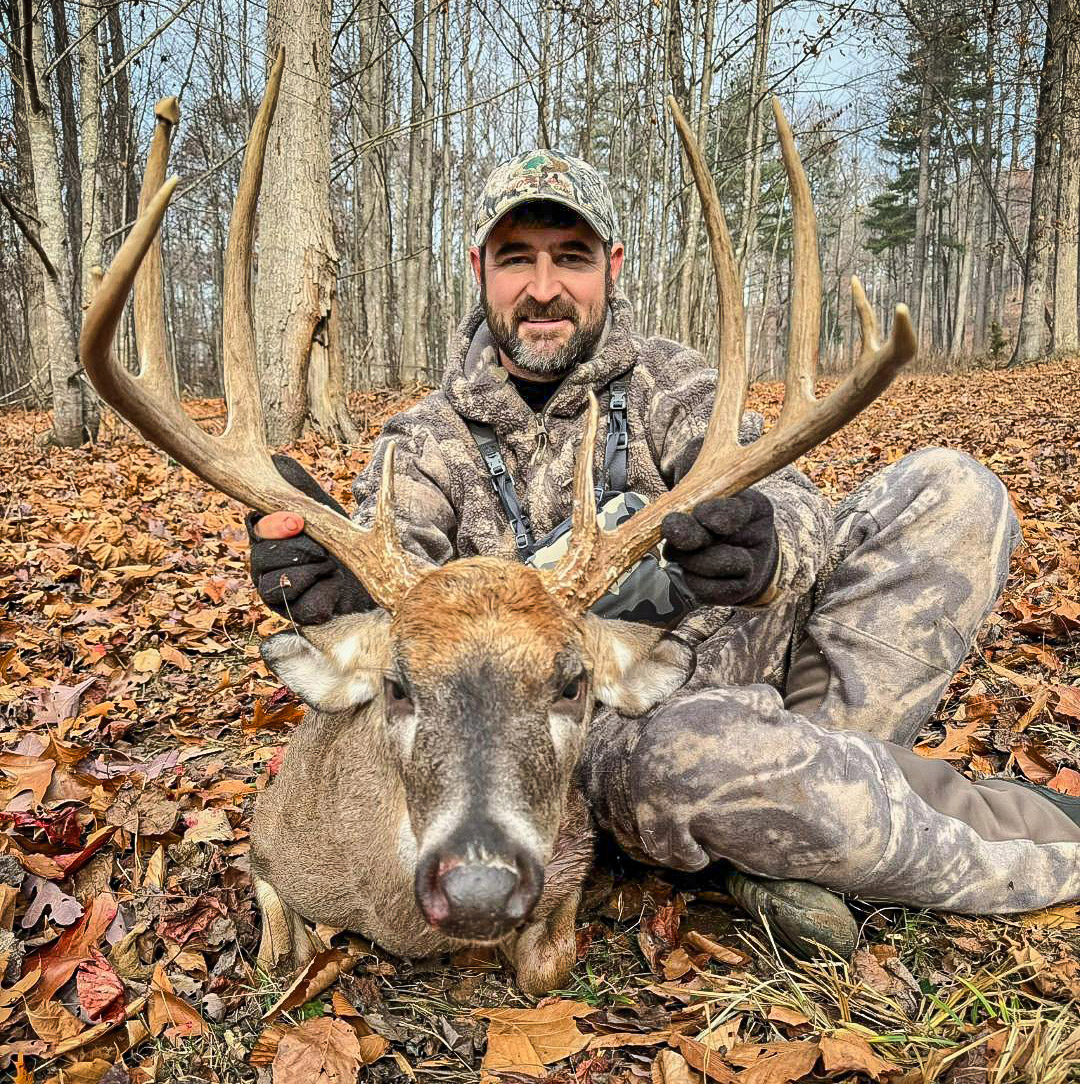 صورة لرجل يرتدي ملابس مموهة ويقف أمام غزال أبيض كبير.