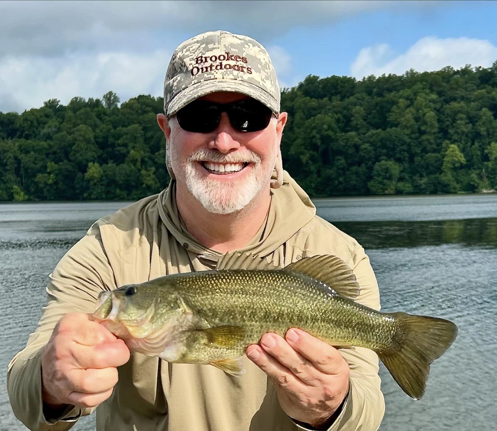 رجل يحمل سمكة باس كبيرة الفم أمام النهر.