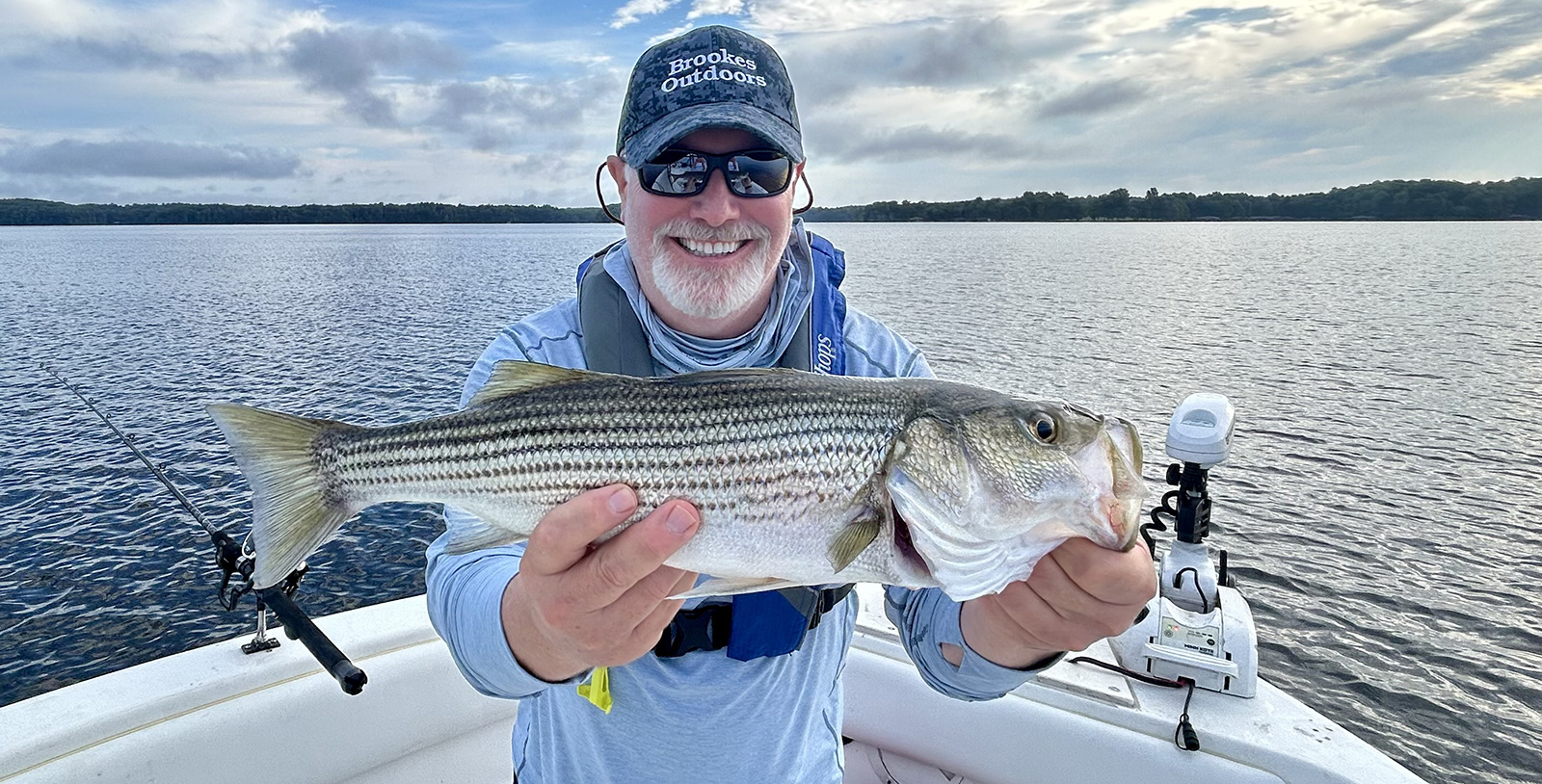 رجل يجلس على متن قارب ويحمل سمكة سمك القاروس المخطط الكبير ويبتسم.