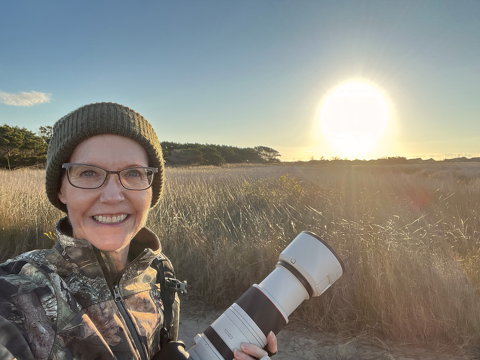 صورة لامرأة تحمل كاميرا عند شروق الشمس بجوار مستنقع.