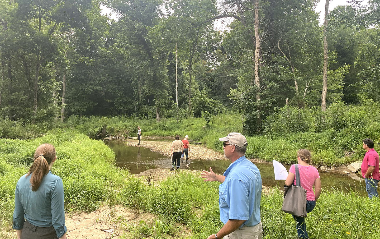 مجموعة من الناس يتجمعون على ضفاف مجرى مائي ويتناقشون.
