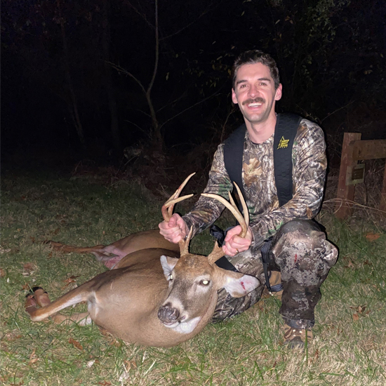 A photo of a man in camouflage holding the antlers of a deer lying down.